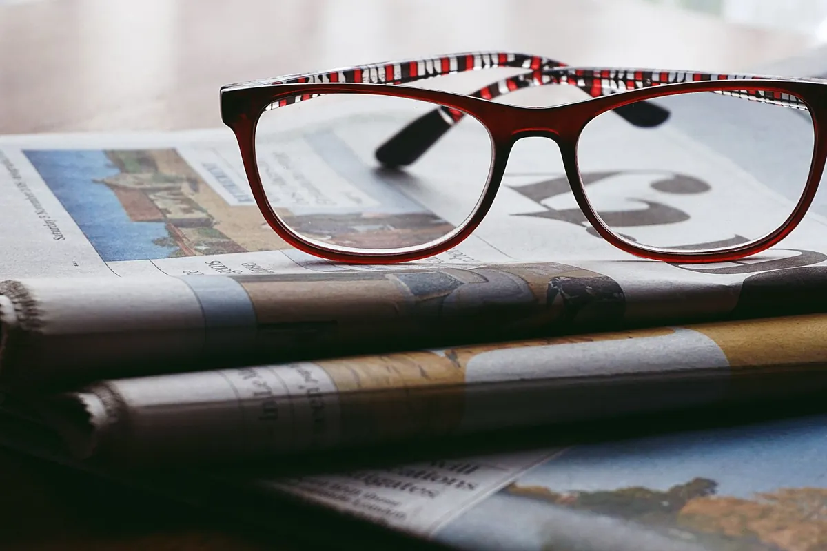Red reading glasses resting on a stack of newspapers