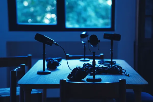 Empty table with four microphones and headphones in a dim, blue-lit room